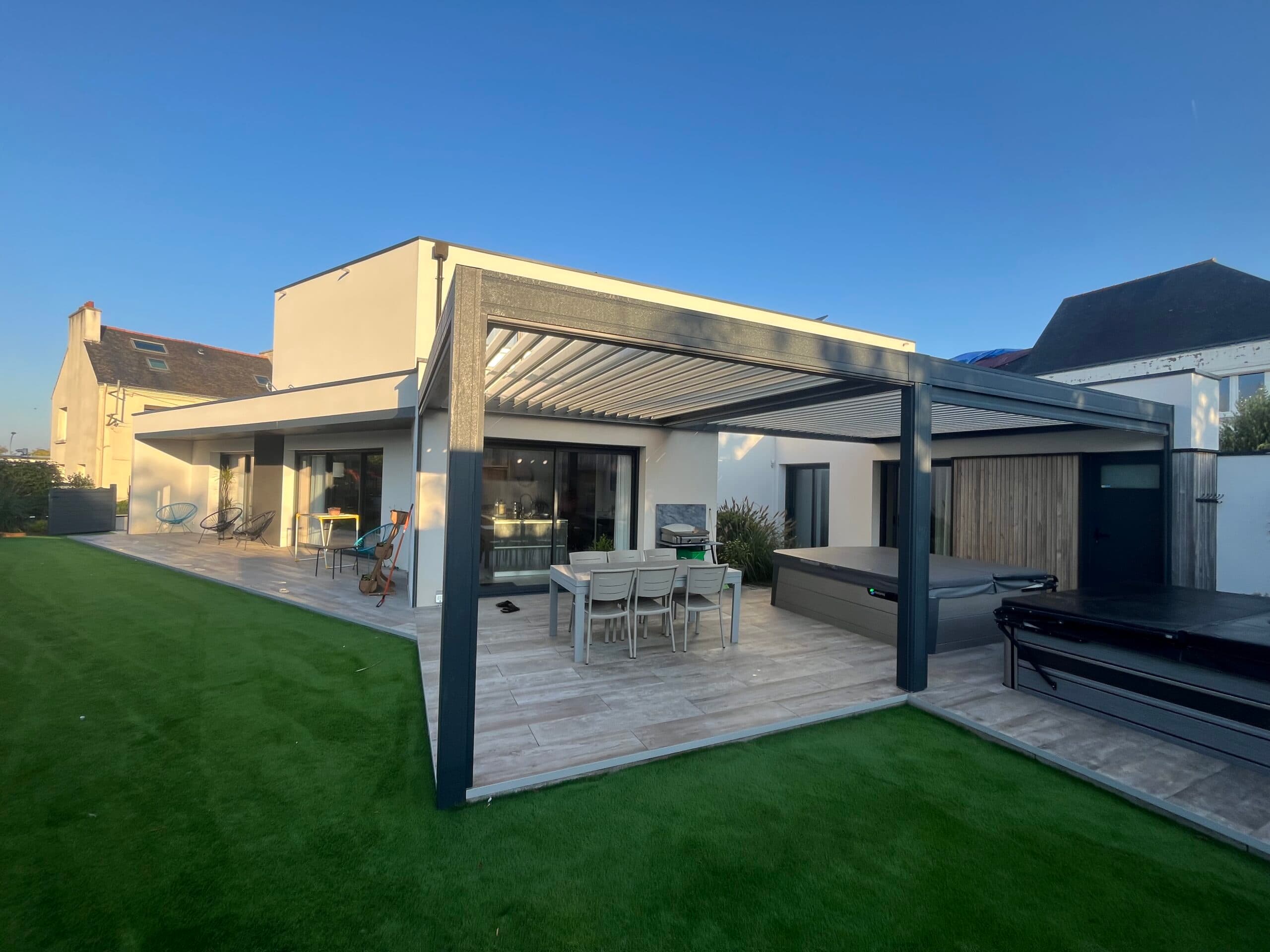 Maison contemporaine avec grande terrasse carrelée, pergola bioclimatique et spa, réalisée par AJY Maçonnerie en bord de mer dans le Morbihan.