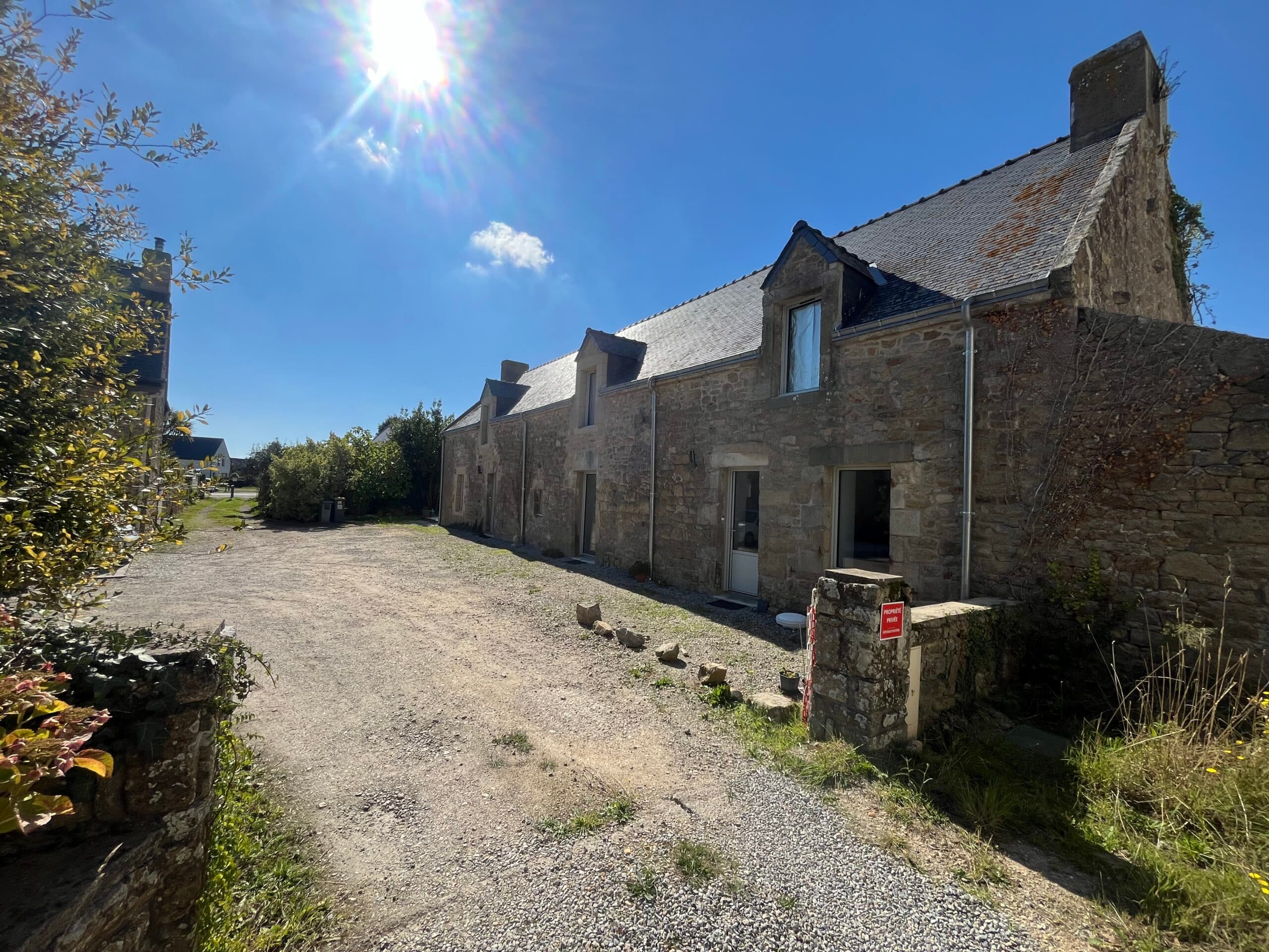 Vue d’ensemble d’une bâtisse en pierre rénovée par AJY Maçonnerie, donnant sur une cour gravillonnée en plein cœur de village breton.
