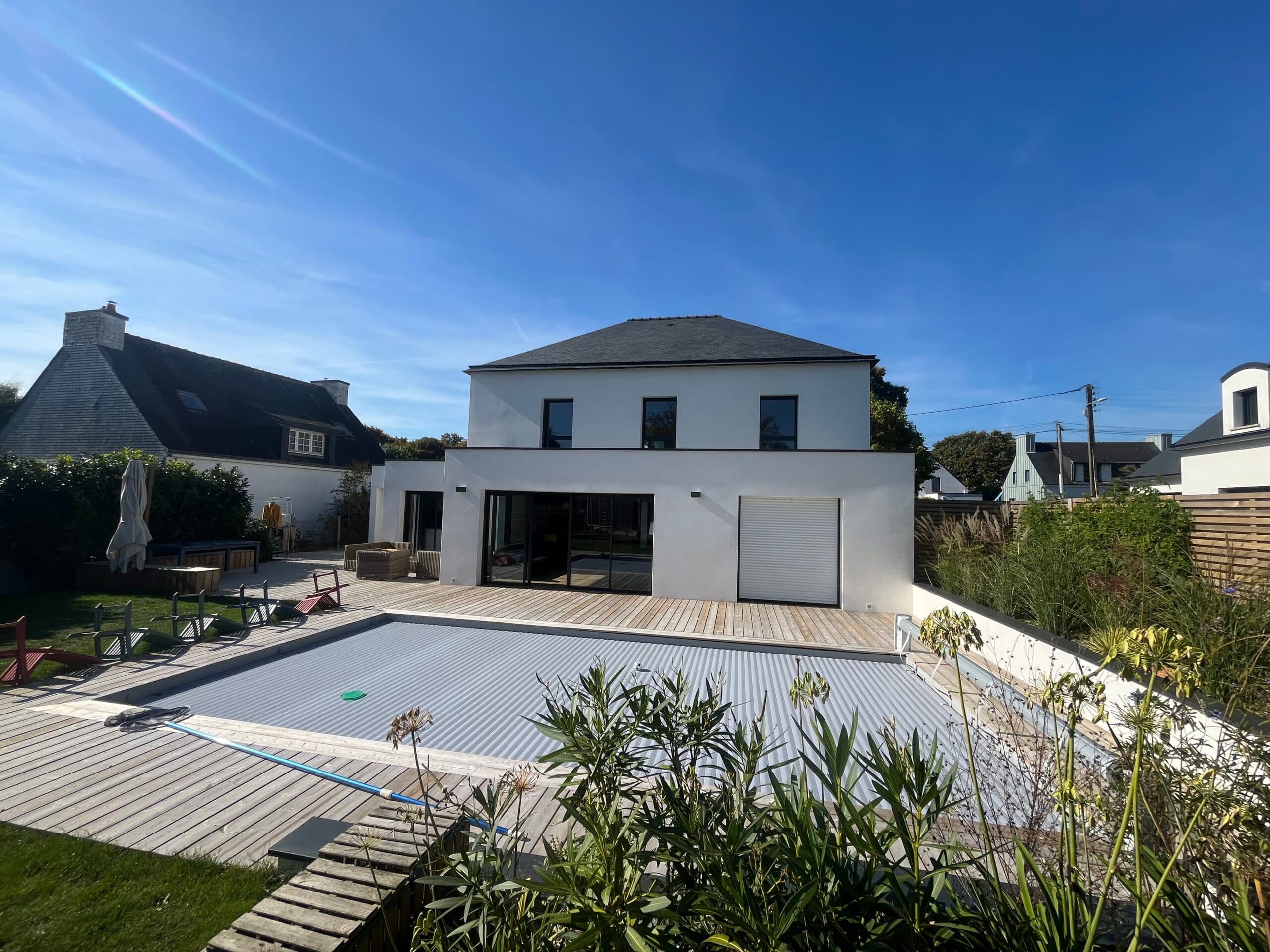 Terrasse en bois d’une maison contemporaine avec grandes baies vitrées, avancée architecturale et coin repas extérieur ensoleillé