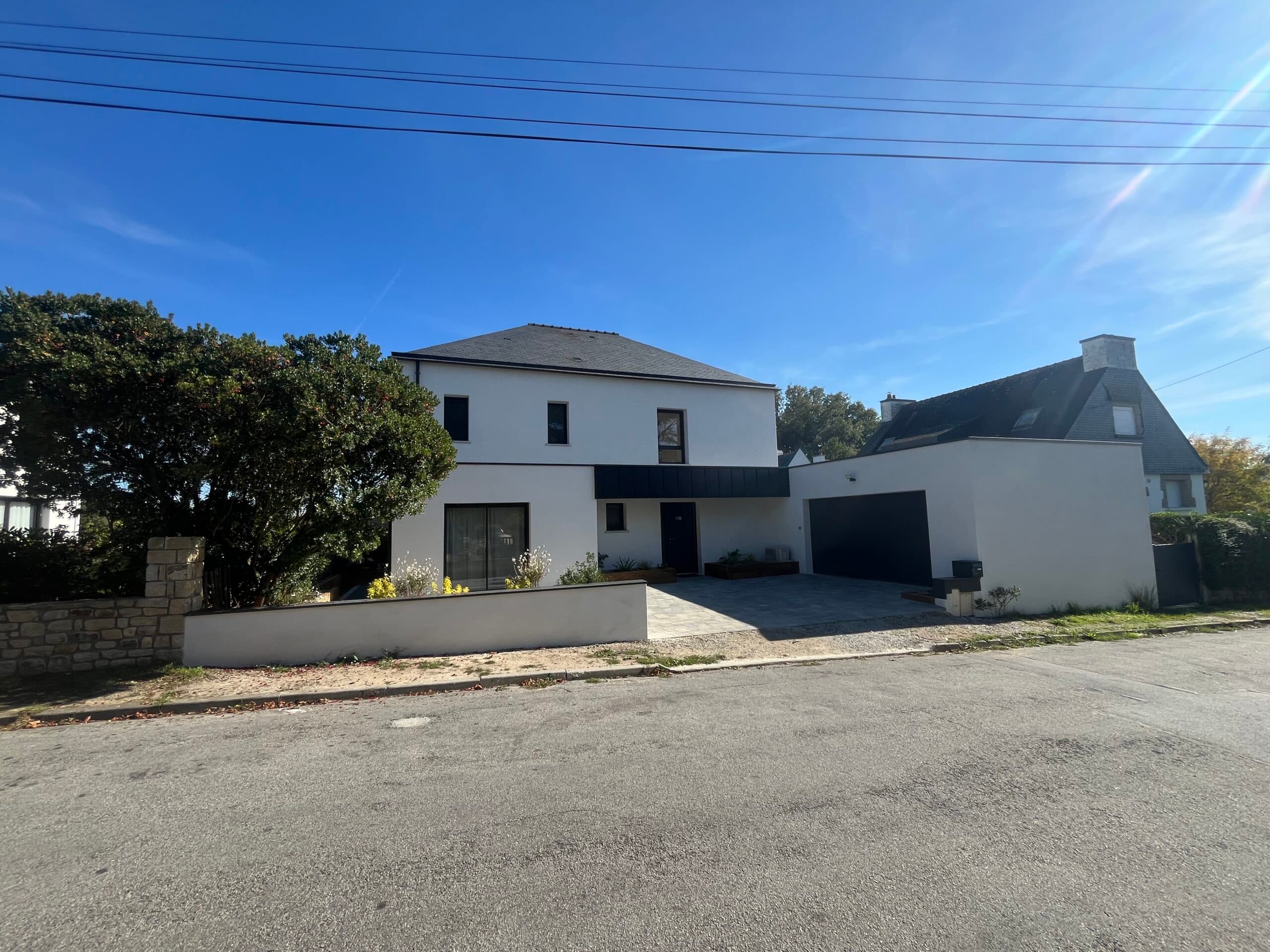 Entrée latérale de maison contemporaine avec grand mur blanc, portail moderne et allée de stationnement en béton