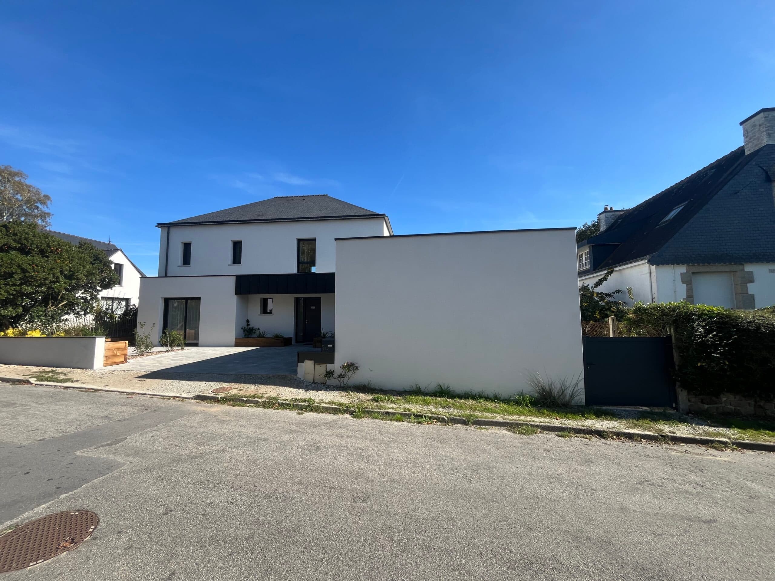 Façade avant de maison moderne toit ardoise avec garage double, cour pavée et mur d’enceinte blanc dans un quartier résidentiel