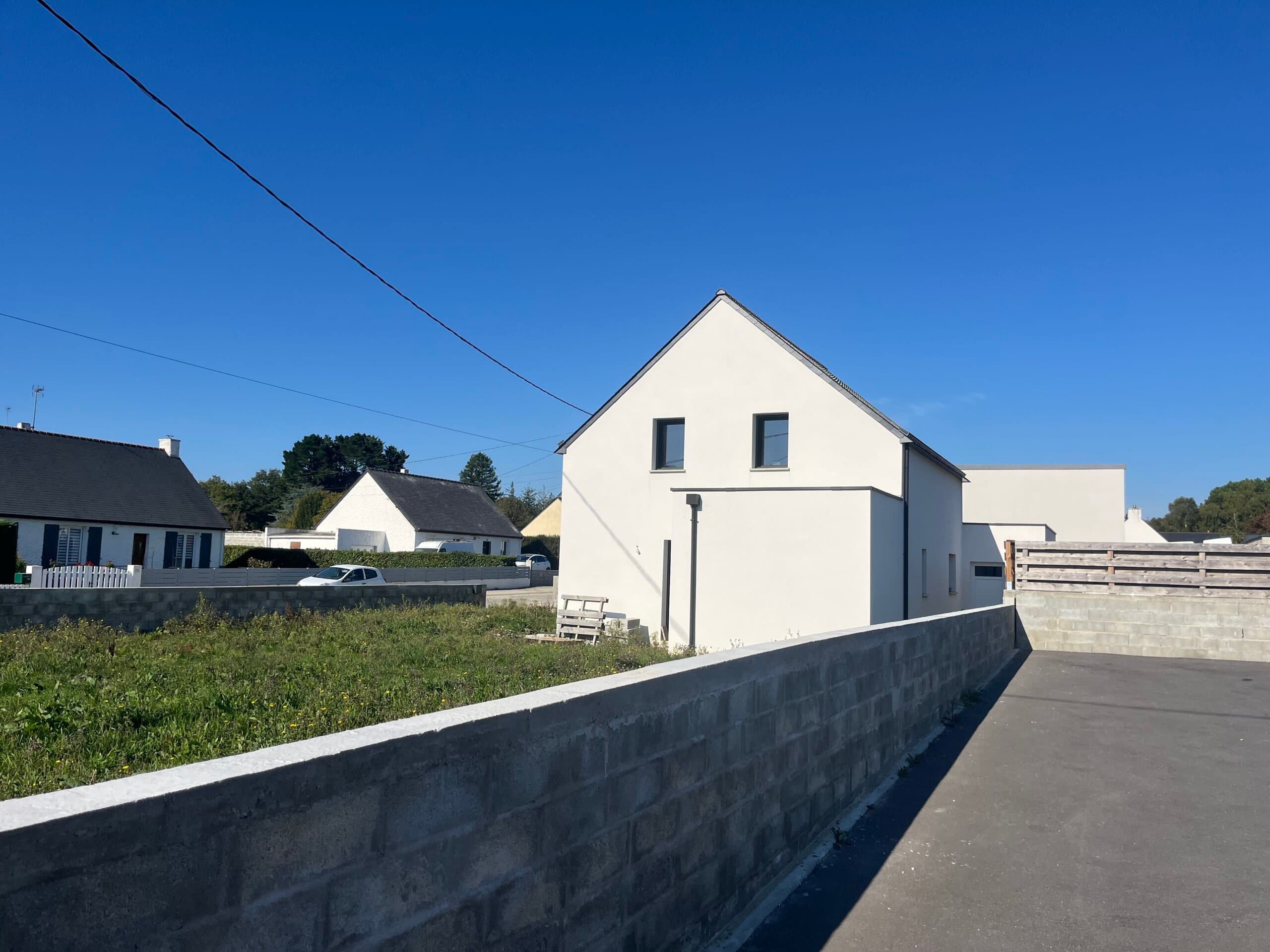 Façade latérale de maison neuve enduite blanc avec mur de clôture en parpaings construite par AJY Maçonnerie.